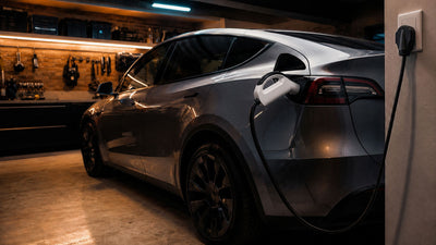 Tesla Model Y parked in a home garage with a portable Level 2 EV charger cable connected via NACS inlet, home charging setup scene